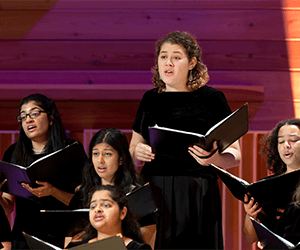 Women wearing black and holding music folders as they sing.