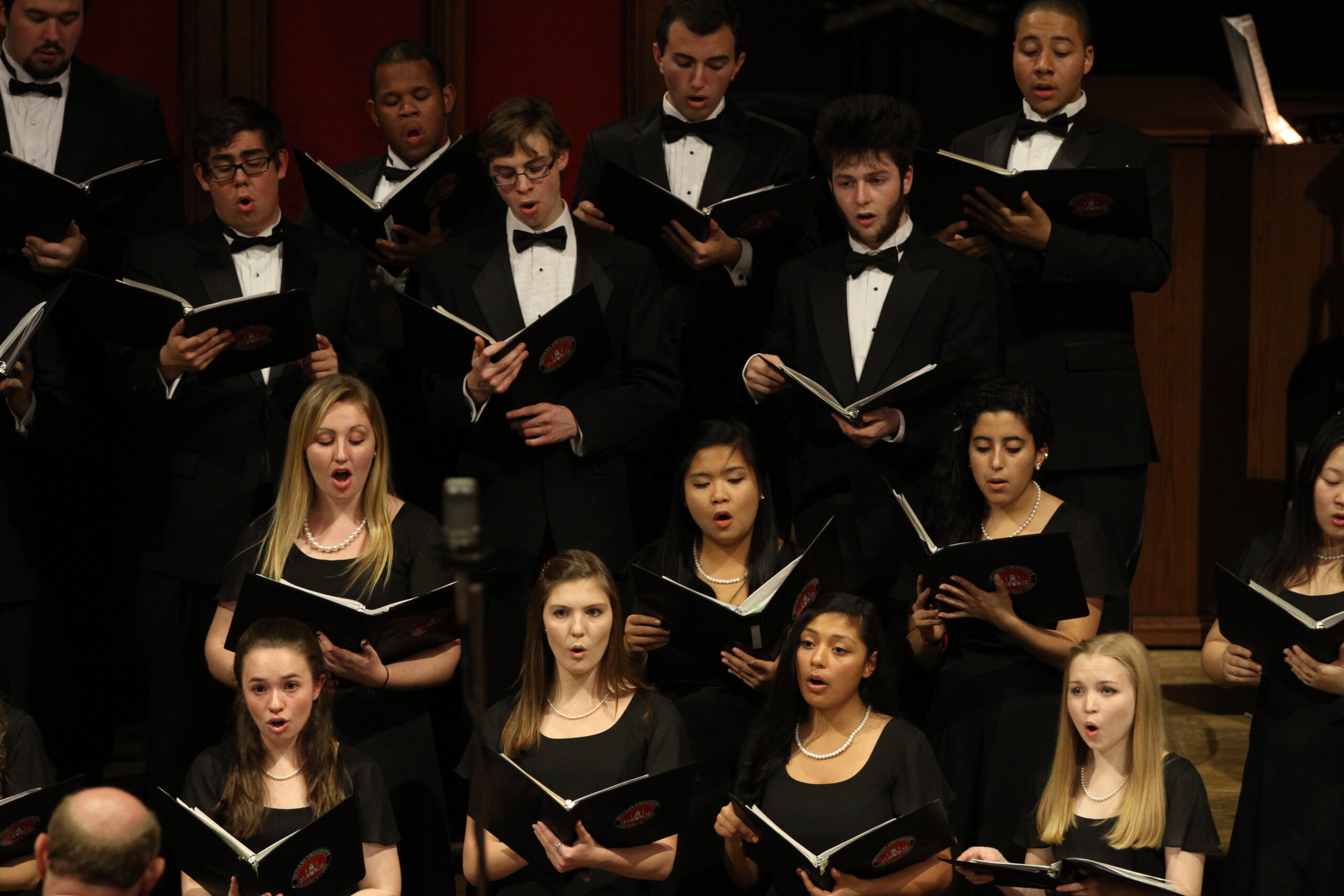 A group of students perform in a choir. They are all wearing formal choral attire. 