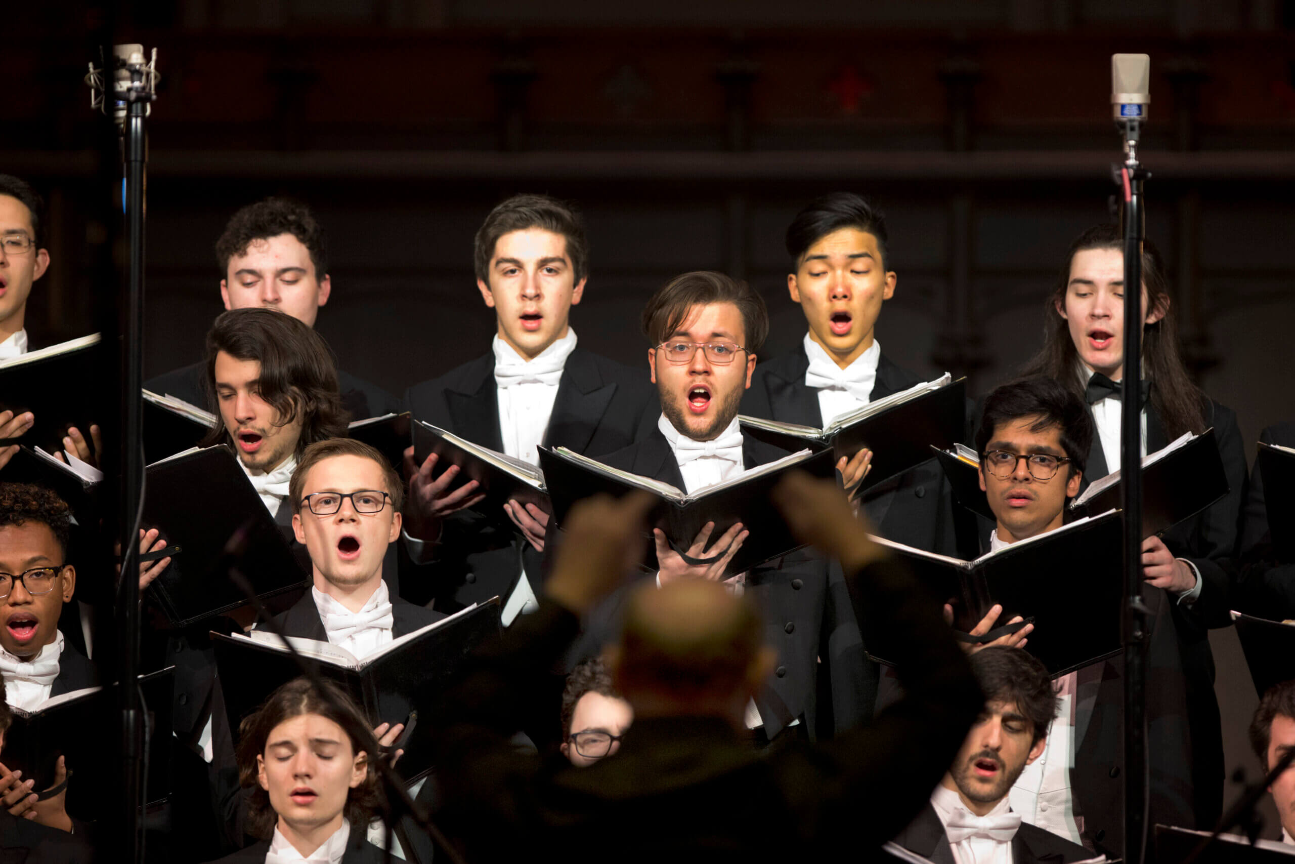 Male choir singers dressed in black and white are singing while holding black music folders.