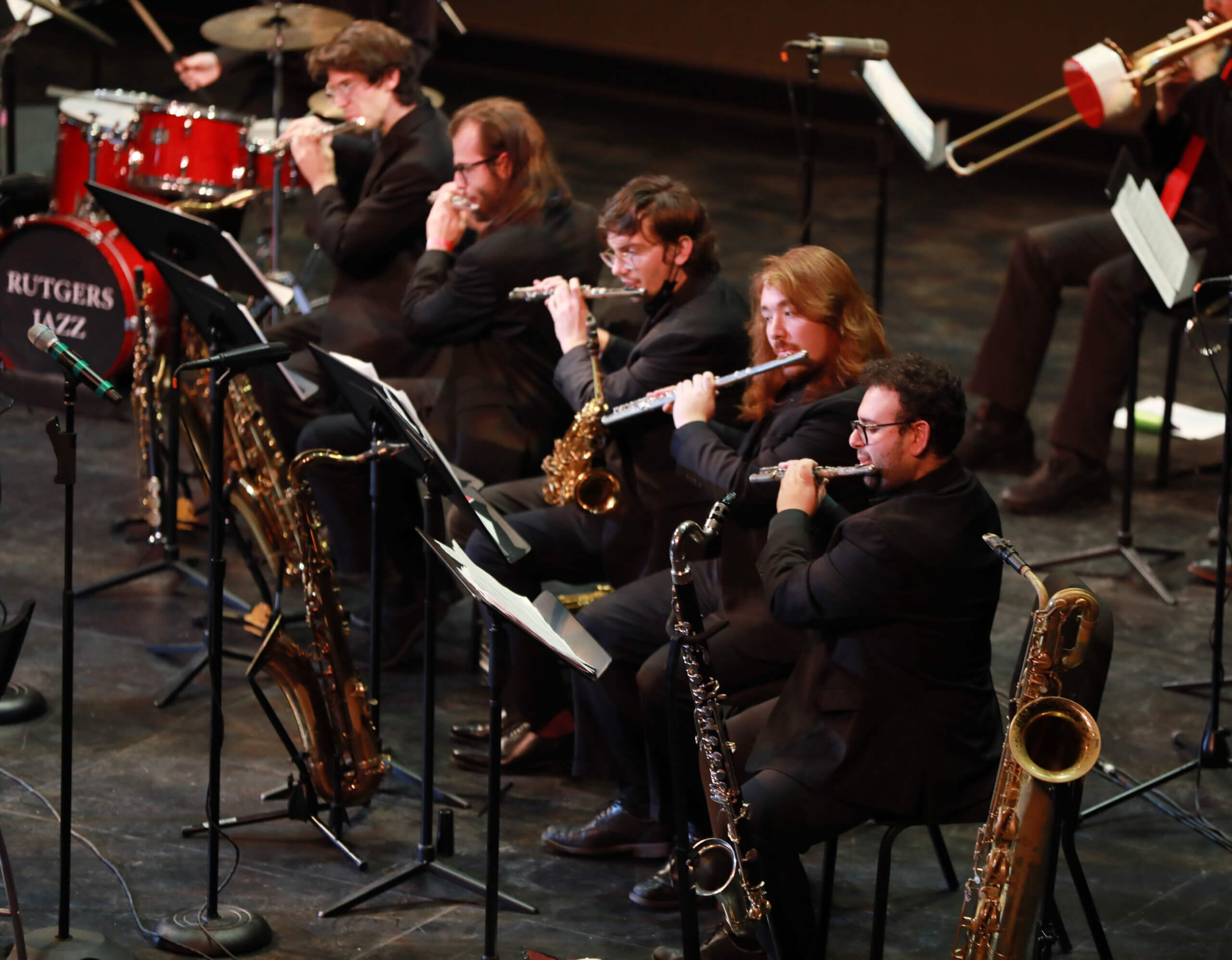 Five students in all black play various instruments on stage.