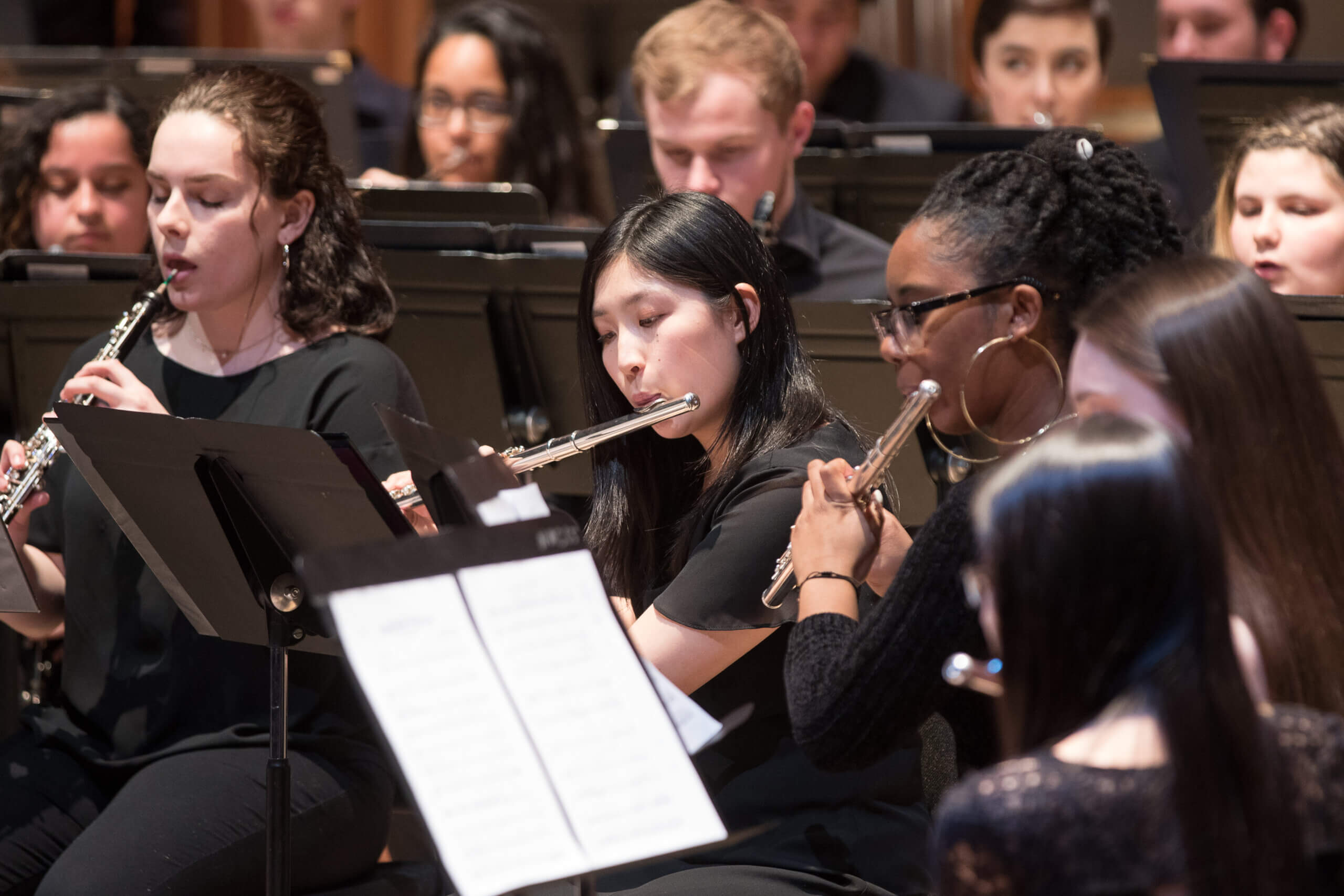 Students perform the flute and other wind instruments on stage.