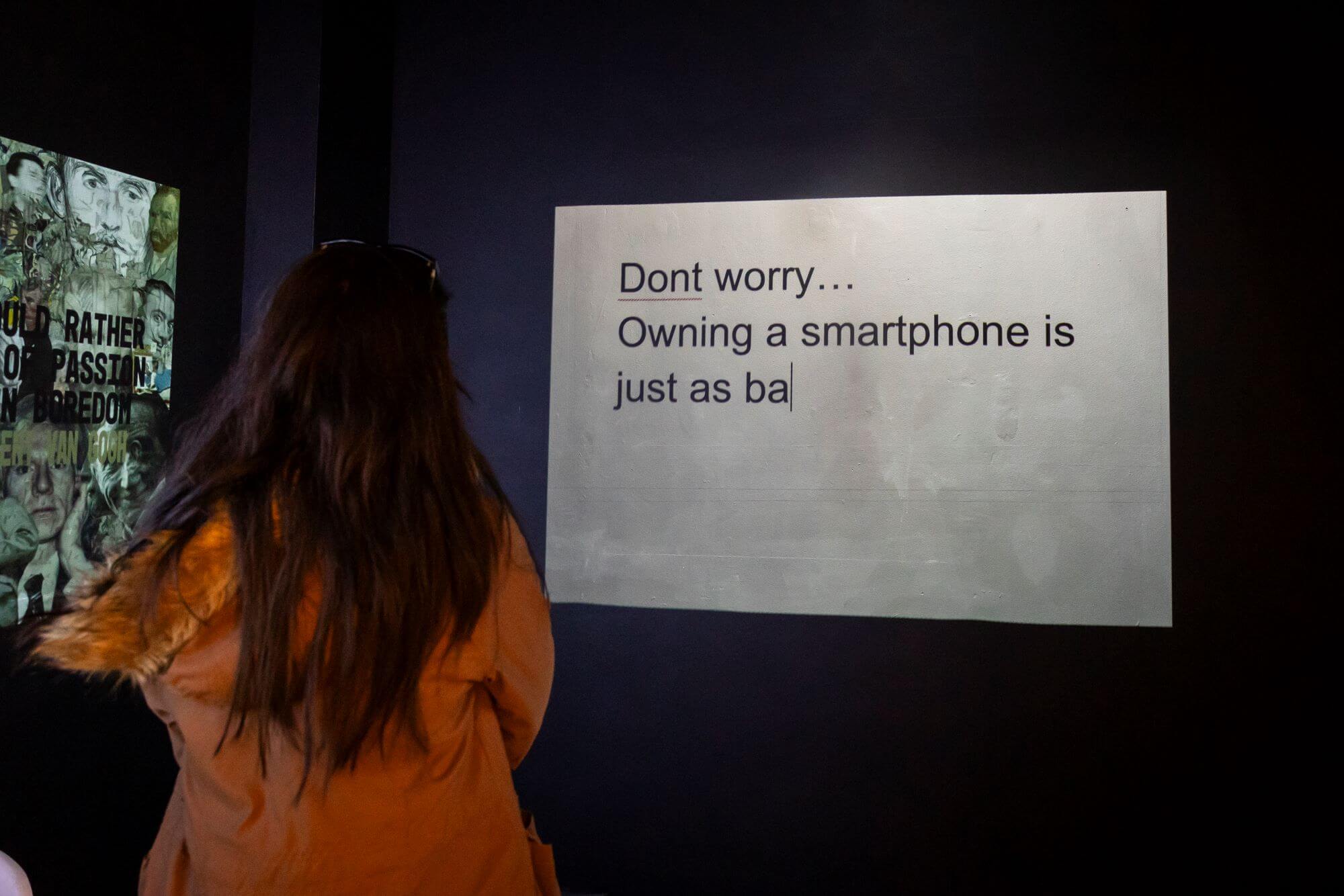 A person in a coat with long hair, their back to the camera, looking at a screen that says: "Don't worry... Owning a smartphone is just as ba