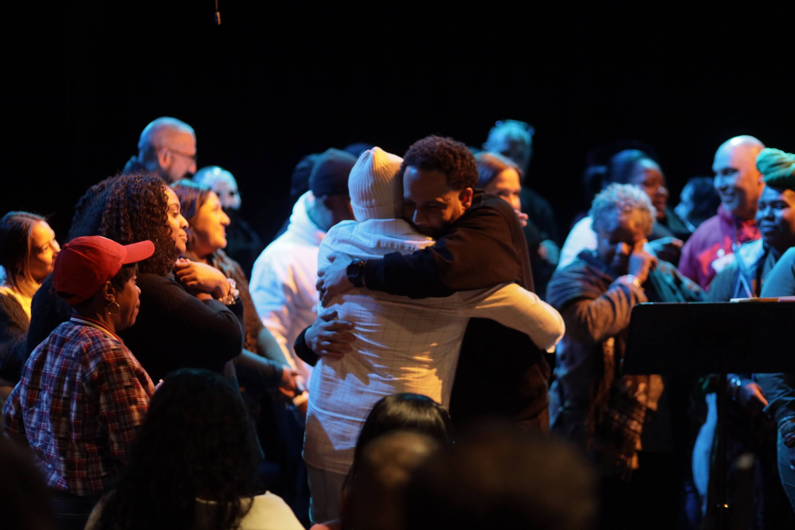 Two people hug in a group of people surrounding them.