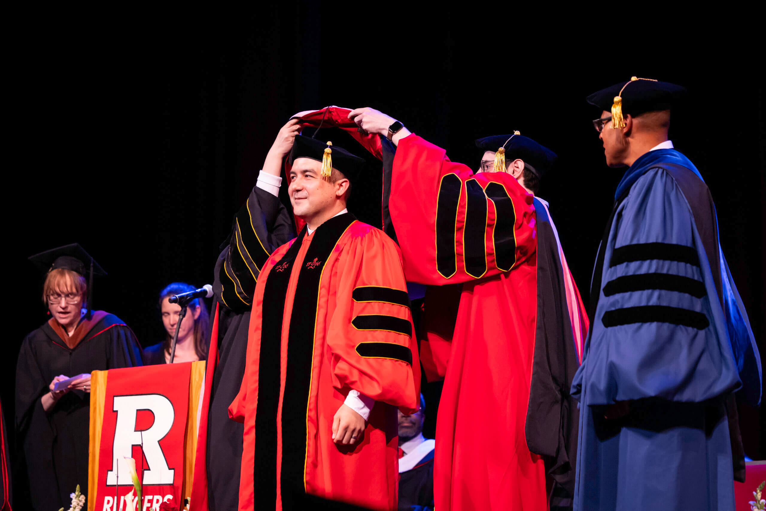Graduates in their caps and gowns sitting at their convocation clapping their hands.
