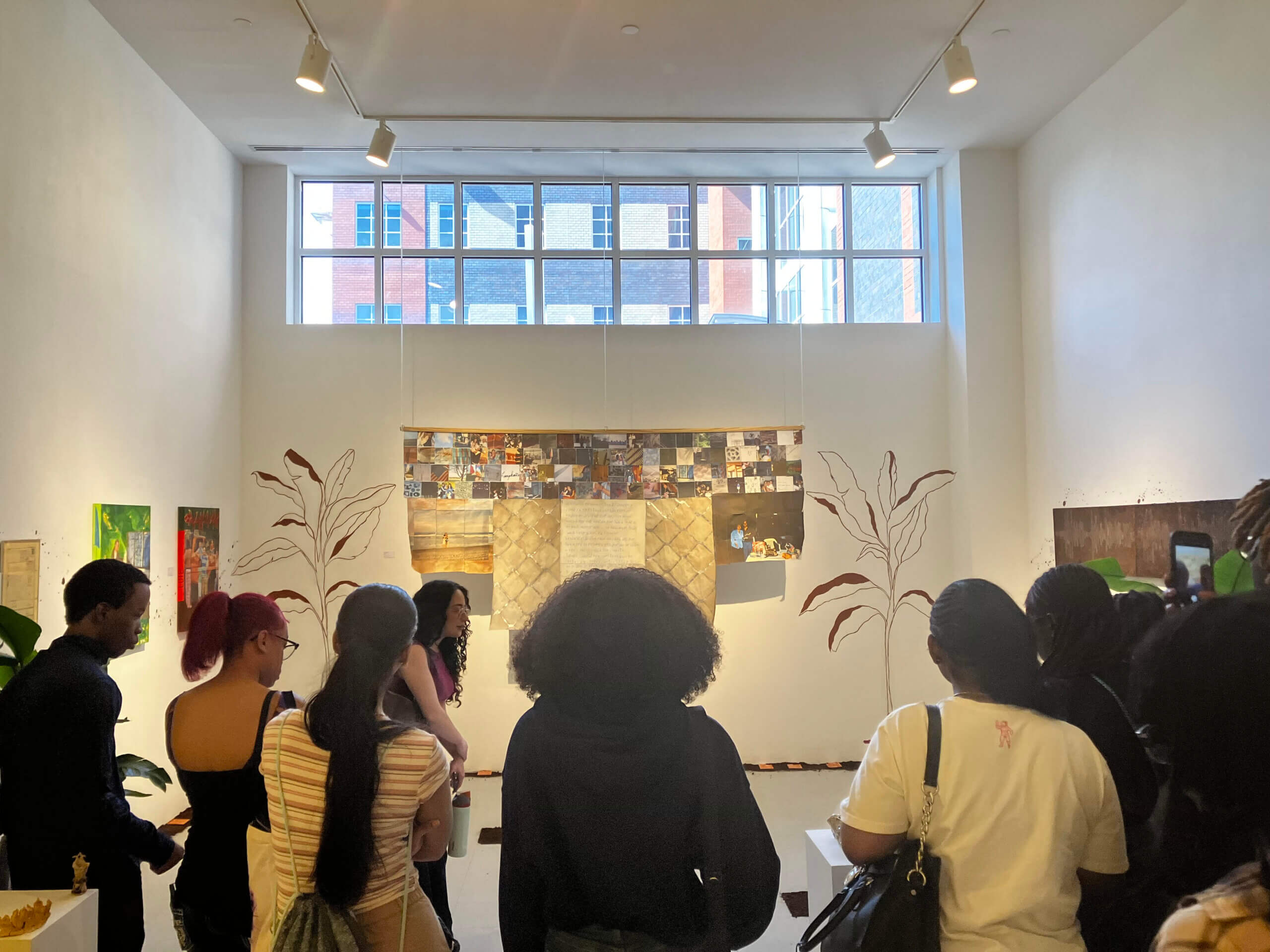Students in a gallery looking at a wall with windows at the top and artwork on the wall below.