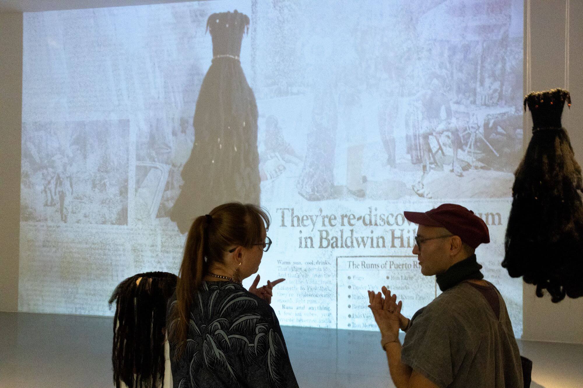 Two people speaking in front of a projected image in a gallery.
