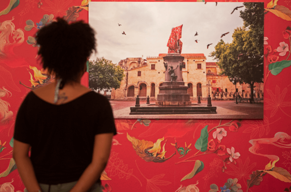 A person stands, looking at an artwork on a red, patterned wall.